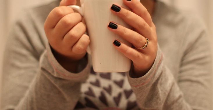 Kobieta z kubkiem herbaty w zadbanych paznokciach